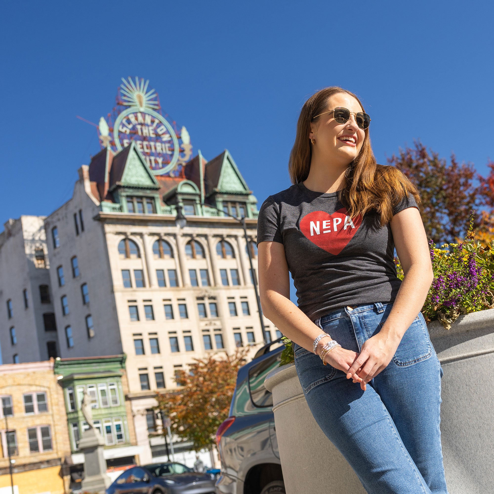 Model wearing Women’s Dark Grey Heather Love NEPA Tee in front of the Electric City sign in Scranton, PA.